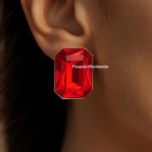 May include: A close-up of a red, rectangular stud earring with a gold-colored frame. The earring has a faceted, gem-like appearance. The text "ProactivWorldwide" is visible on the earring.