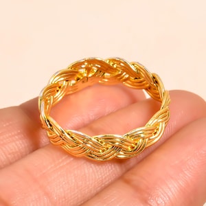Peut inclure: Une bague dorée avec un motif tressé. La bague est faite d'un matériau métallique brillant et présente un motif tissé. La bague est un bijou.