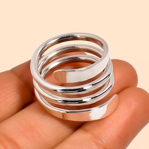 Puede incluir: Un anillo en espiral plateado con un acabado pulido. El anillo se enrolla alrededor del dedo varias veces, creando un efecto en capas. El diseño es simple y moderno, adecuado para el uso diario.