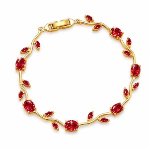 May include: A gold bracelet with a vine design, adorned with red oval gemstones and leaf-shaped details. The bracelet, with a clasp closure, is set against a white backdrop. The gemstones are approximately 1 cm in length.