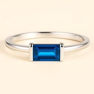 May include: A silver ring with a rectangular, deep blue gemstone. The gemstone is set between two silver bars, offering a modern design. The ring band is smooth and polished. This piece of jewellery is suitable for everyday wear or special occasions.