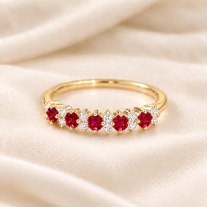 Könnte beinhalten: Ein Goldring mit einer Reihe von fünf runden roten Rubinen, die sich mit Paaren kleiner, klarer, runder weißer Diamanten abwechseln. Die Steine sind in einer Krappenfassung entlang der oberen Hälfte des polierten Gelbgoldbandes gefasst.