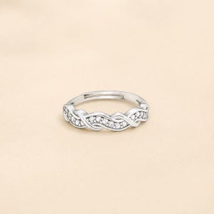 Op de afbeelding: Een zilverkleurige ring met een open, verstelbaar bandontwerp en een gedraaid, verweven patroon. Het oppervlak van de ring is versierd met een reeks kleine, heldere, rondgeslepen stenen die in het midden van de gedraaide metalen strengen zijn gezet.