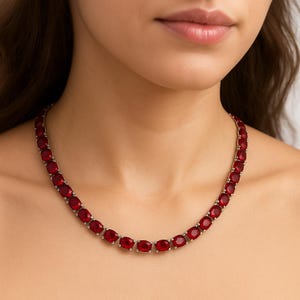 Op de afbeelding: Een zilveren ketting met een reeks ovale, dieprode edelstenen. De edelstenen zijn gelijkmatig verdeeld en gezet in zilvermetaal. De ketting is een klassiek ontwerp, geschikt voor formele of casual kleding.