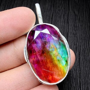 May include: Oval pendant featuring a multicoloured gemstone. The gem showcases a spectrum of colours, including red, purple, yellow, and green, set in a silver metal frame. The pendant has a loop for a chain.