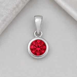 Könnte beinhalten: Silberanhänger mit einem runden, facettierten, leuchtend roten Edelstein. Der Anhänger hat ein schlichtes, elegantes Design mit poliertem Finish. Der Edelstein ist in einer Lünettenfassung gefasst.