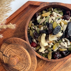 Könnte beinhalten: Ein hölzernes Serviertablett mit sechseckiger Form, das eine Holzschale mit einer Mischung aus Nüssen und Trockenfrüchten enthält. Das Tablett hat einen Deckel und ein dekoratives Design. Das Tablett ist aus rotbraunem Holz.