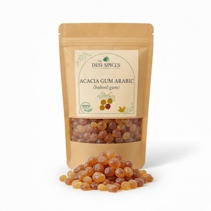 Peut inclure: Un sac en papier brun contenant de la gomme arabique d'acacia (gomme babool) de The Desi Spices, avec une étiquette indiquant le nom du produit et un symbole de 100 %. Le sac est rempli de petits morceaux de gomme ronds et ambrés, avec un tas de la même gomme devant.