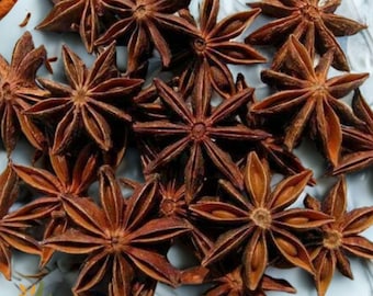 May include: Close-up of star anise spices. The star-shaped pods are a deep reddish-brown color, with a textured surface. The spices are scattered on a light blue surface. The image is well-lit, highlighting the details of the spice.