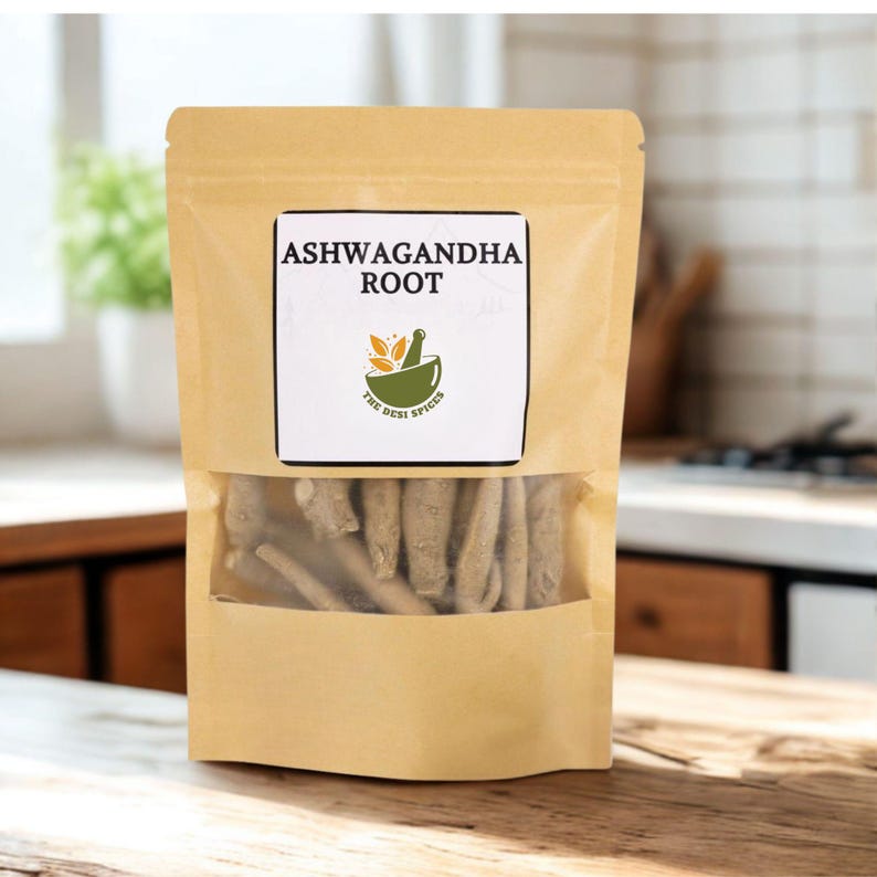 May include: A tan paper bag with a clear window displaying ashwagandha root. The bag has a white label with the text "ASHWAGANDHA ROOT" and a green and orange logo. The bag is sitting on a wooden surface.