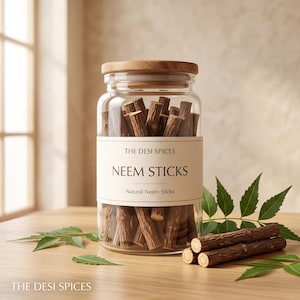 Könnte beinhalten: Ein durchsichtiges Glasgefäß mit Holzdeckel, gefüllt mit braunen Neem-Stäbchen. Das Etikett trägt die Aufschrift THE DESI SPICES NEEM STICKS Natural Neem Sticks. Zwei lose Neem-Stäbchen und grüne Neem-Blätter liegen vor dem Glasgefäß.