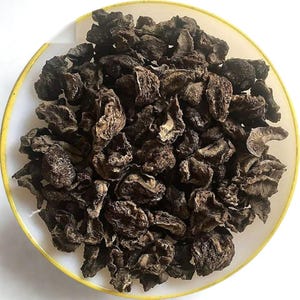 Puede incluir: Primer plano de un plato blanco con borde amarillo lleno de trozos secos, marrón oscuro, de forma irregular. Los trozos parecen ser un tipo de fruta o verdura seca, posiblemente para uso culinario.