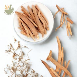 May include: A top-down shot of ashwagandha roots, some on a white plate and others scattered on a white surface. The roots are a light brown color and have a slightly rough texture. The Desi Spices logo is in the upper left corner.