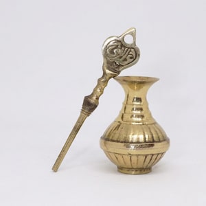 May include: A vintage brass kohl eyeliner applicator and container. The applicator has an ornate handle and a decorative top. The container is a small, round vase with vertical ridges. The items are gold-colored and sit against a white background.