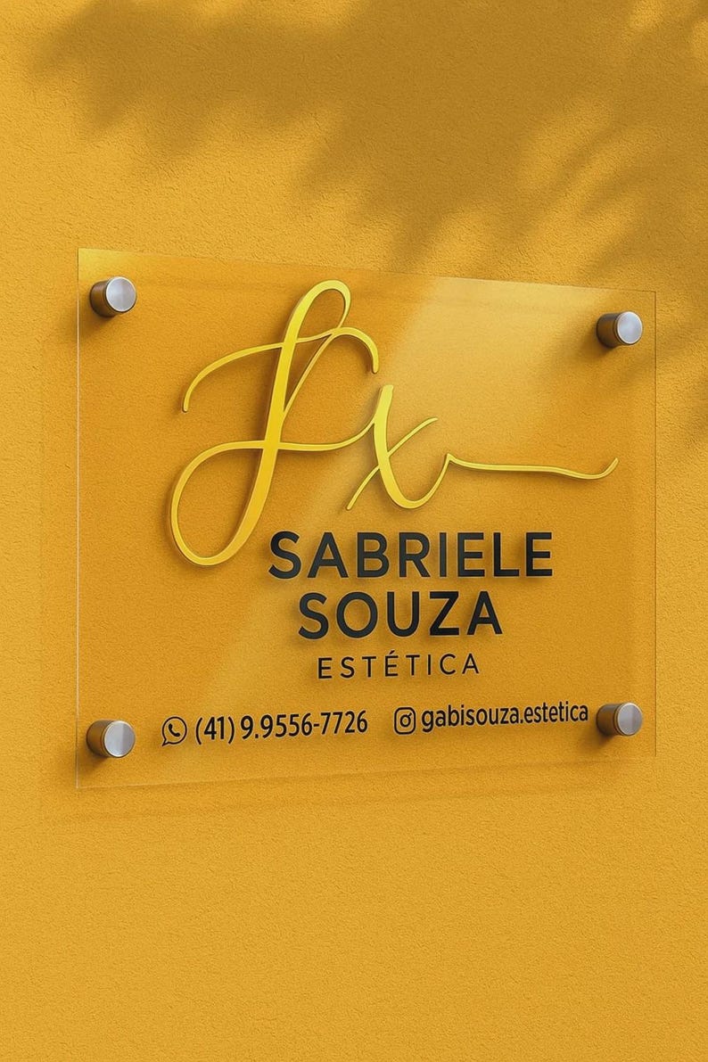 K&ouml;nnte beinhalten: Klarer Acrylschild mit goldfarbenen Buchstaben und silbernen Befestigungen. Das Schild zeigt "Sabriele Souza Est&eacute;tica" mit Telefonnummer und Instagram-Handle. Der Hintergrund ist einfarbig gelb.