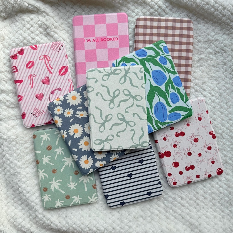 Puede incluir: Una colecci&oacute;n de cuadernos estampados con varios dise&ntilde;os. Los cuadernos presentan patrones como cuadros rosas, margaritas, cerezas, lazos y rayas. Un cuaderno tiene el texto "I'M ALL BOOKED". Los cuadernos est&aacute;n dispuestos sobre una superficie blanca texturizada.