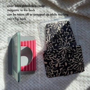 Puede incluir: Un lector electr&oacute;nico con borde verde menta, una funda a rayas rosas y rojas y una funda con estampado floral negro y beige. El texto de la imagen dice: tapa trasera transparente desmontable, magn&eacute;tica en la parte trasera, se puede quitar o apoyar mientras se lee, no se puede plegar.
