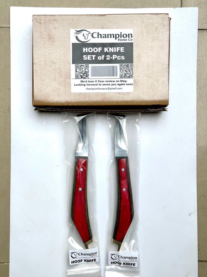Pu&ograve; includere: Un set di due coltelli per zoccoli, ciascuno con un manico in legno rosso e una lama argentata, confezionati in plastica trasparente. I coltelli sono di Champion Horse Co. La scatola sopra i coltelli riporta la scritta "HOOF KNIFE SET of 2-Pcs".