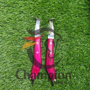May include: Two knives with bright pink wooden handles and silver blades are displayed against a green background. The handles have a dark wood grain pattern and are accented with brass details. The blades are curved.