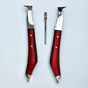 Pu&ograve; includere: Tre strumenti da maniscalco: due coltelli per zoccoli con manici in legno rosso e una piccola raspa in metallo. I coltelli hanno una lama curva e dettagli in ottone. Il testo "championhorseshoe@gmail.com" &egrave; stampato sulla lama.