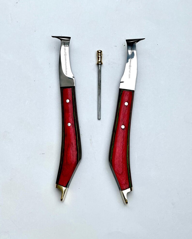 Pu&ograve; includere: Tre strumenti da maniscalco: due coltelli per zoccoli con manici in legno rosso e una piccola raspa in metallo. I coltelli hanno una lama curva e dettagli in ottone. Il testo "championhorseshoe@gmail.com" &egrave; stampato sulla lama.
