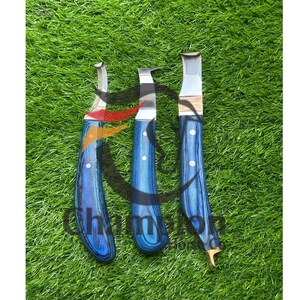 May include: Three metal carving tools with blue wood grain handles. The blades are silver and curved, with a sharp edge. The handles are a vibrant blue with a wood grain pattern. The tools are arranged on a bed of green grass.