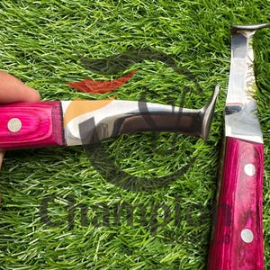 May include: Two hoof knives with bright pink wooden handles and silver blades. One knife has a curved blade, the other has a straight blade. The handles are secured with silver rivets. The knives are designed for farrier work.