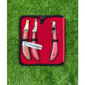 May include: A set of three hoof knives with curved metal blades and pink wooden handles, secured in a red-lined black zippered case. A white tag attached to the handles features the text Champion Horse Co with a horse head logo.
