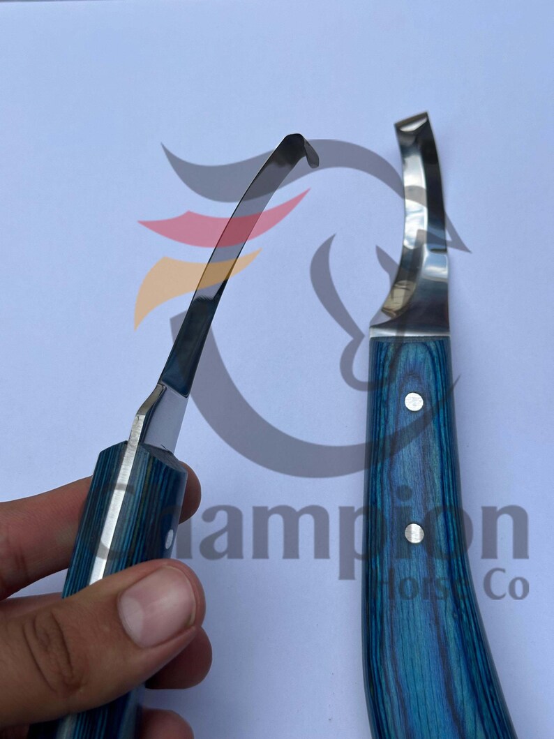 May include: Two hoof knives with blue and silver handles are displayed against a white background. The blades are curved and shiny. The handles have a blue wood grain pattern. One knife is held in a hand.