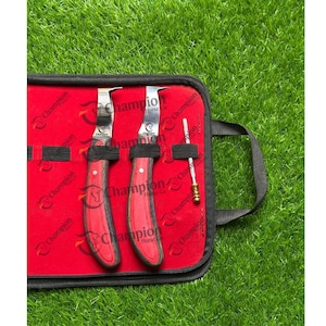 May include: A red and black Champion Horse Co. hoof knife set in a black zippered case. The set includes two hoof knives and a small tool, all with the Champion Horse Co. logo. The case is open, revealing the tools against a red interior.