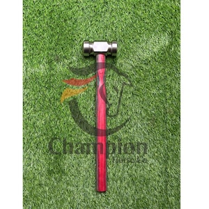 May include: A metal hammer with a red wooden handle. The hammer head is silver and rectangular. The handle is a vibrant red with dark wood grain. The word "Champion" is printed on the green background.