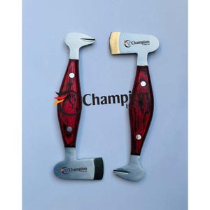 Op de afbeelding: Twee hoefsmedengereedschappen met houten handvatten en zilveren bladen. De handvatten zijn donkerrood met een houtnerfpatroon. De bladen hebben het woord "Champion" erop gedrukt. De gereedschappen zijn voor hoefverzorging.