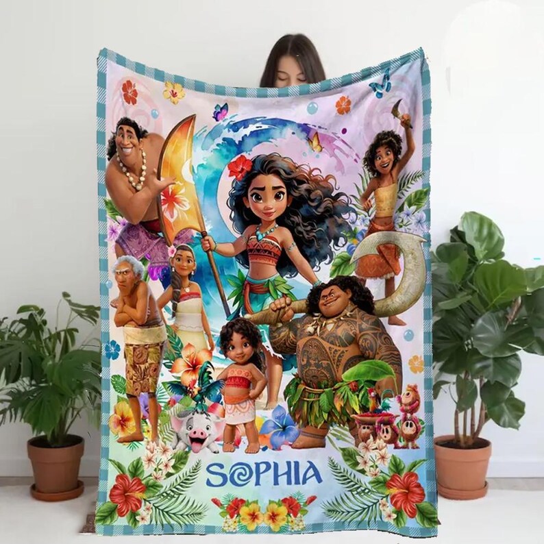 May include: A colorful fleece blanket featuring characters from the animated movie Moana. The blanket has a blue and white checkered border and includes the name "Sophia" in a script font. The design includes images of Moana, Maui, and other characters.