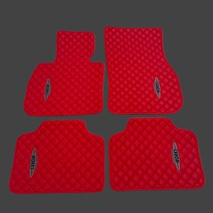 May include: Set of four red car floor mats with a diamond-quilted pattern. Each mat features the text "WORKS" in a silver and black emblem. The mats are designed to fit a vehicle's interior.