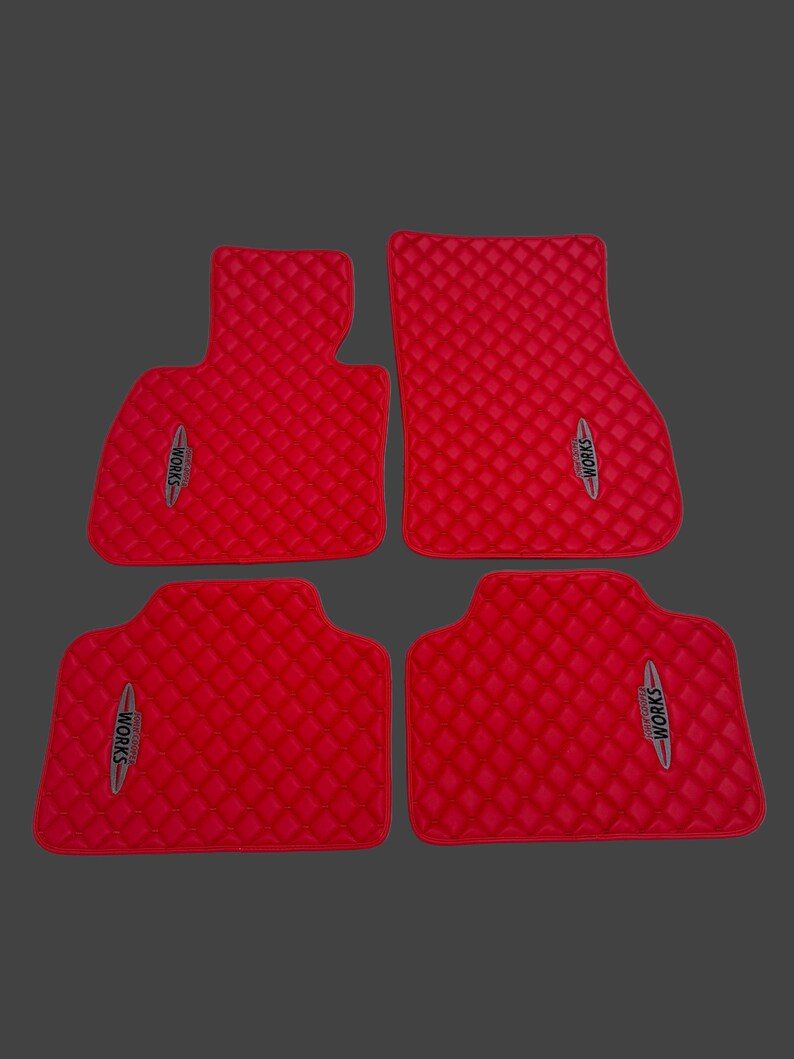 May include: Set of four red car floor mats with a diamond-quilted pattern. Each mat features the text "WORKS" in a silver and black emblem. The mats are designed to fit a vehicle's interior.