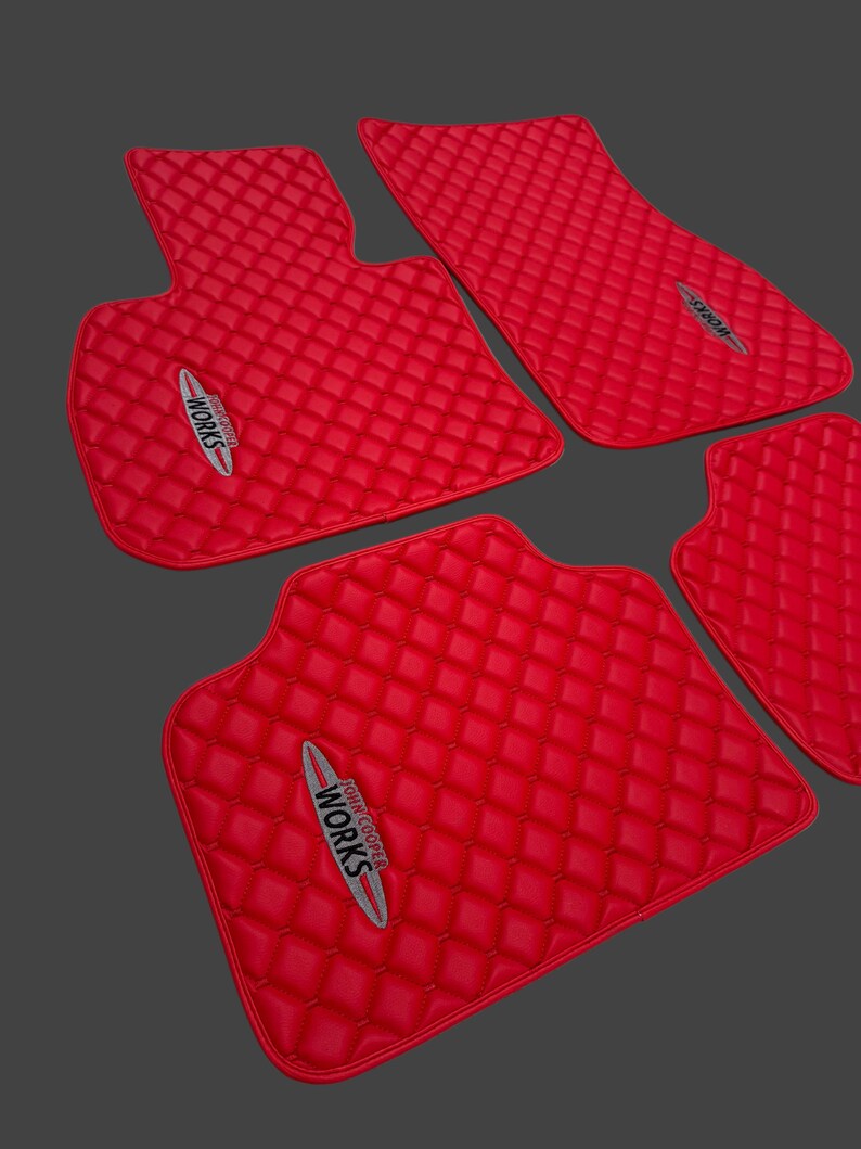 May include: Set of four bright red car floor mats with a diamond-quilted pattern. Each mat features the "John Cooper Works" logo in white, red, and gray. The mats are designed to fit a car's interior.