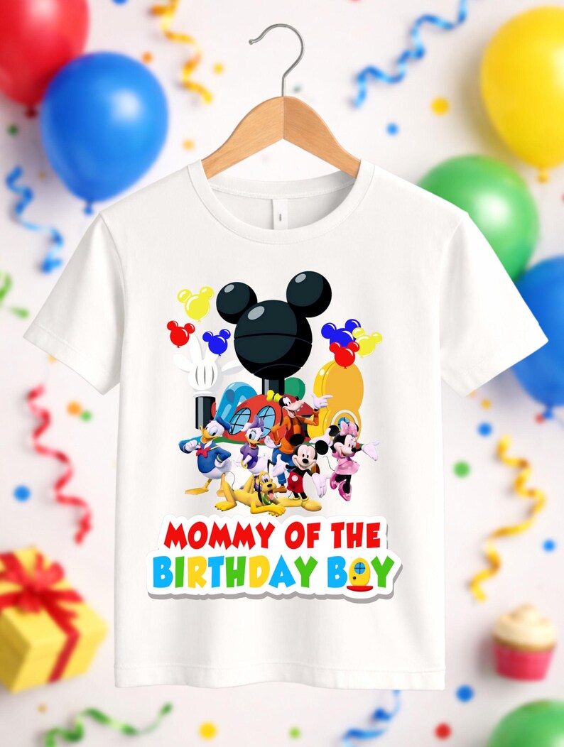 May include: A white short-sleeved t-shirt featuring a colorful graphic of various cartoon characters including Mickey Mouse, Minnie Mouse, Donald Duck, and Pluto. The text "MOMMY OF THE BIRTHDAY BOY" is printed in red, yellow, blue, and green letters.