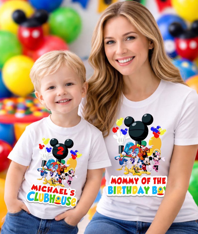 May include: Two white t-shirts featuring a colorful graphic of Mickey Mouse and friends. The smaller shirt displays the text "MICHAEL'S CLUBHOUSE" with a red number two, while the larger shirt displays the text "MOMMY OF THE BIRTHDAY BOY".