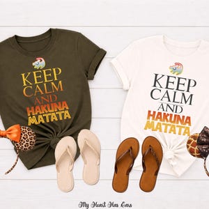 Peut inclure: Deux t-shirts avec l'inscription "Keep Calm and Hakuna Matata" en noir et orange. Les accessoires comprennent des oreilles de Minnie Mouse à imprimé léopard et girafe, et des tongs neutres. Les chemises sont vert olive et blanches.