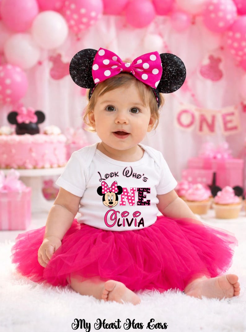 May include: A baby wearing a white onesie with a Minnie Mouse graphic and the text "Look Who's ONE Olivia". The baby is wearing a pink tutu and a Minnie Mouse ear headband with a pink bow. Pink balloons and a cake are in the background.