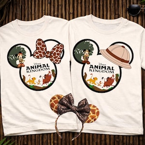 May include: Two white t-shirts with Disney's Animal Kingdom graphics. One features a Minnie Mouse bow with a giraffe print, the other a safari hat. A matching headband with giraffe print ears and a sequined bow is also visible.