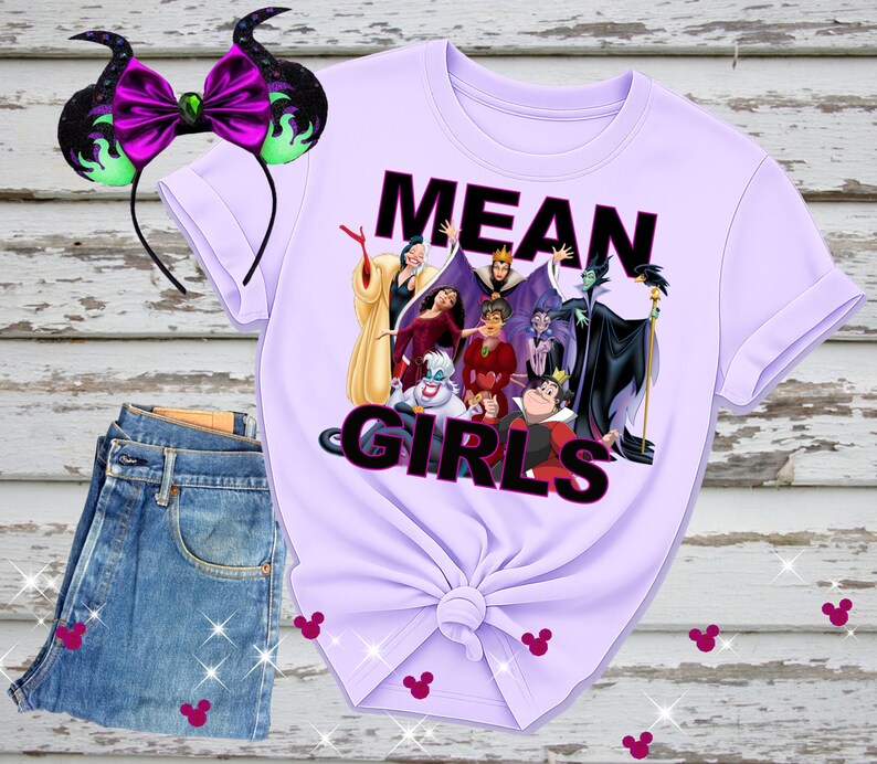 K&ouml;nnte beinhalten: Ein helllila T-Shirt mit dem Text "MEAN GIRLS" und einer Grafik von Disney-B&ouml;sewichten. Ein passendes Stirnband mit lila Schleife und schwarzen H&ouml;rnern befindet sich links. Blaue Jeans sind darunter gefaltet.