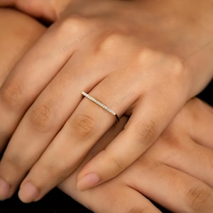 May include: A gold-toned ring featuring a straight bar design, encrusted with small, sparkling diamonds. The ring is worn on a finger, showcasing its delicate and minimalist aesthetic. The ring's design is simple yet elegant, suitable for everyday wear or special occasions.