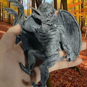 May include: A gray gargoyle figurine with large wings, pointed ears, and a textured surface. The statue is in a climbing pose, with arms outstretched. The gargoyle is a decorative item, possibly for a garden or home decor.