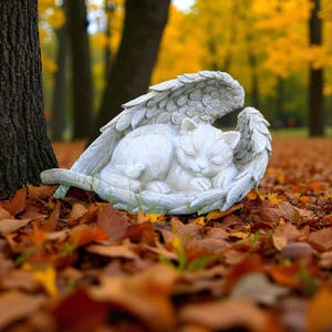 May include: A white cat sculpture with angel wings, resting peacefully. The cat is curled up, nestled within the wings, creating a serene and comforting scene. The sculpture is set outdoors among fallen autumn leaves.