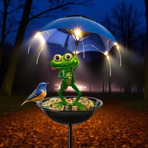 May include: A novelty garden bird feeder. A green frog figure holds a blue umbrella with lights. A blue and orange bird perches on the edge of the feeder. The feeder is filled with birdseed and is mounted on a black pole.