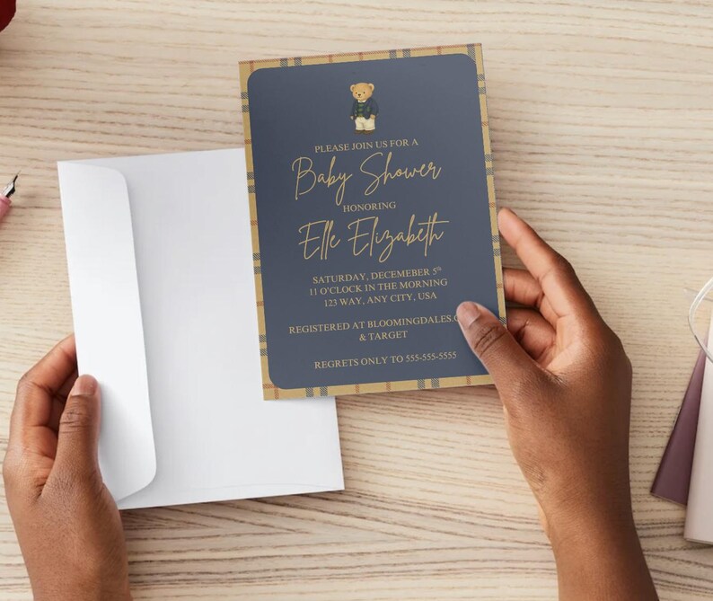 May include: A baby shower invitation with a navy blue background and gold text. The invitation features a teddy bear illustration and a plaid border. The text reads "Please join us for a Baby Shower honoring Elle Elizabeth."