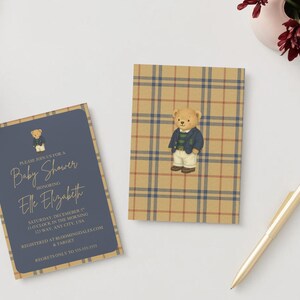 May include: Baby shower invitations featuring a teddy bear illustration. One invitation has a navy blue background with gold text and a teddy bear graphic. The other invitation has a plaid pattern with a teddy bear graphic. A gold pen and flowers are also in the image.