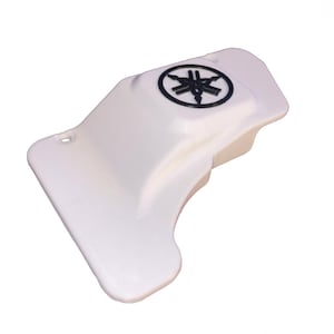 May include: A white motorcycle part with a black Yamaha logo. The part has a curved shape with a flat edge and a small hole. The Yamaha logo is a black emblem.