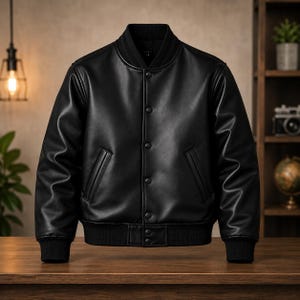 Peut inclure: Une veste de style universitaire noire en matière lisse, dotée d'un col, de poignets et d'un ourlet côtelés. La veste comprend une fermeture à boutons-pression sur le devant, deux poches latérales inclinées et des manches longues.